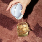 Hand pouring liquid from a small container into a glass on a textured surface