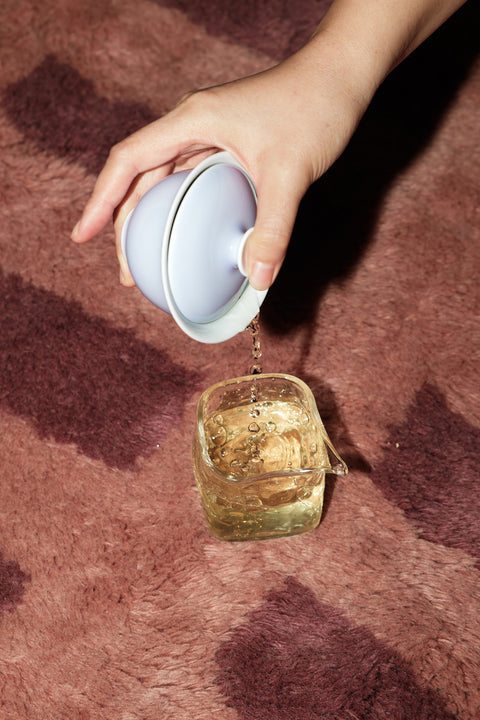 Hand pouring liquid from a small container into a glass on a textured surface