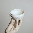 Hand holding a small ceramic bowl against a plain background